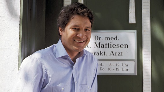 Dr. Mattiesen (Christian Quadflieg) steht in der Fernsehserie "Der Landarzt" vor seinem Praxis-Schild. © picture-alliance / KPA 