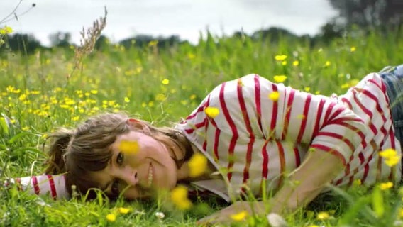 Anneke Kim Sarnau liegt auf einer Blumenwiese und schaut in die Kamera. © NDR 