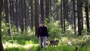 Wotan Wilke Möhring spaziert mit einem Korb in der Hand neben einem Wolf durch einen Wald © NDR 