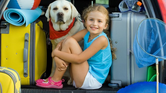 Ein Mädchen und ein Hund sitzen in einem voll gepackten Kofferraum © Gorilla - Fotolia Foto: Wojciech Gajda