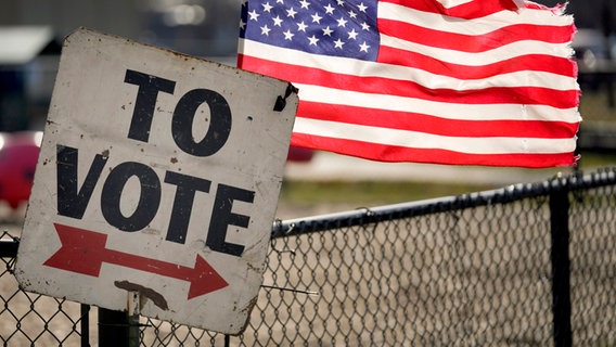 Ein Wahlschild und eine amerikanische Flagge sind vor einem Vorwahlbüro in Dearborn, Michigan zu sehen © dpa Foto: Paul Sancya
