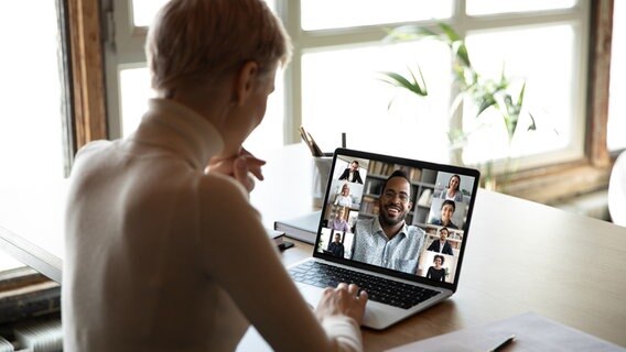 Eine Frau schaut auf einen Monitor, auf dem mehrere Menschen in einer Videokonferenz dargestellt sind. © Colourbox Foto:  Aleksandr