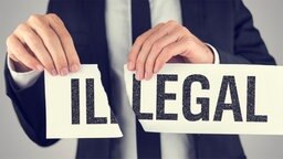 Jemand zerreißt einen Zettel auf dem das Wort Illegal in Legal und Illegal zerteilt wird, Jemand zerreißt einen Zettel auf dem das Wort Illegal in Legal und Illegal zerteilt wird, © fotolia.com Foto: Gajus Schild