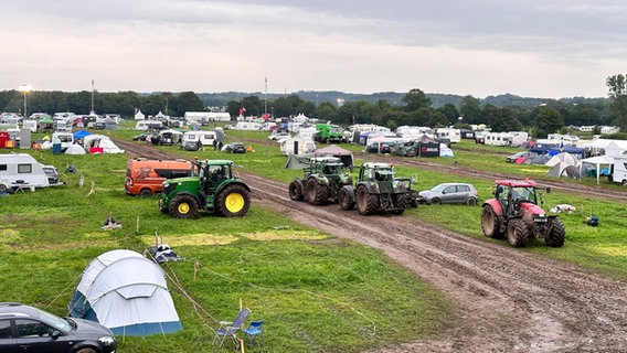 Nach dem Wacken Open Air 2023 fahren am Sonntag mehrere Traktoren über den Campingbereich des Festivals. Einige Wohnwagen und Zelte stehen noch. © NDR 