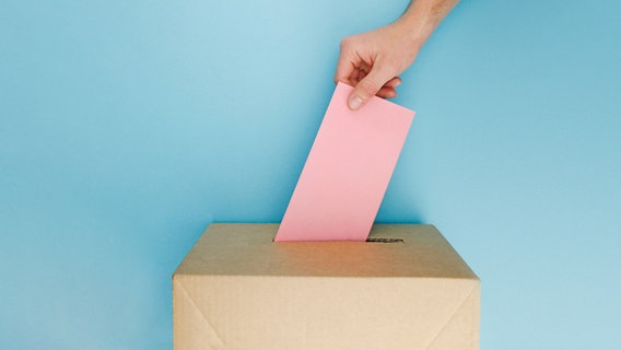 Eine Person steckt einen roten Umschlag in eine Wahlurne aus Pappe © photocase.de Foto: PolaRocket