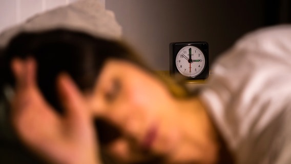 Eine Frau liegt schlafend im Bett, dahinter ist ein Wecker zu erkennen © Christoph Soeder/dpa +++ dpa-Bildfunk Foto:  Christoph Soeder