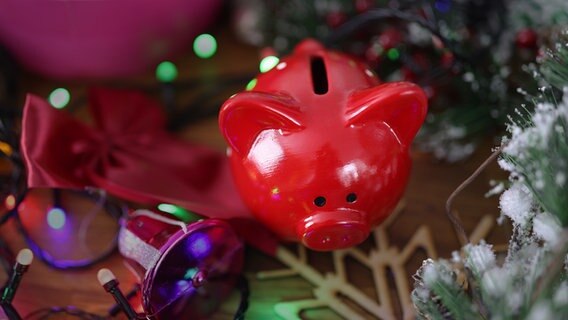 Ein rotes Sparschwein steht auf einem Tisch inmitten von Weihnachtsdeko. © Colourbox Foto: -