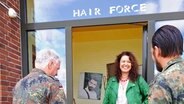 Andrea Storm steht vor ihrem Friseursalon Hairforce und lächelt zwei Soldaten an. © NDR Foto: Ines Barber