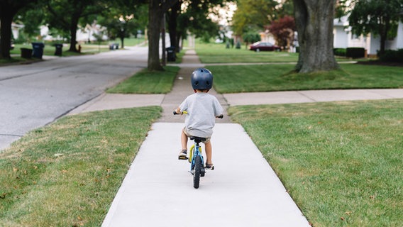 Ein kleiner Junge fährt mit dem Fahrrad auf dem Gehweg. © Imago Foto: Mint Images