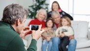 Ein Mann fotografiert mit einem Smartphone seine Familie vor dem Weihnachtsbaum. © fotolia Foto: Tyler Olson