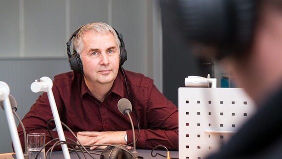 Pastor Friedemann Magaard sitzt mit Kopfhörern vor einem Mikrofon im Studio. © NDR Foto: Janis Röhlig
