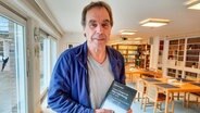 Autor Reinhard Jannen steht mit seinem neuen Buch "Lorenz Friedrich Mechlenburg" in einer Bibliothek © NDR Foto: Karin Haug