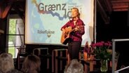 Eine Teilnehmerin des Jugendkongress in Klanxbüll spielt Gitarre, Mundharmonika und singt dazu © NDR Foto: Karin Haug