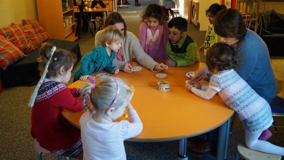Viele Kita-Kinder stehen an Tisch und spielen mit Erzieherin. © NDR Foto: Marie Meyer