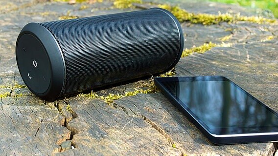 Ein Smartphone liegt neben einen tragbaren Lautsprecher auf einem abgesägtem Baumstumpf. © Fotolia Foto: baloon 111