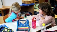 Zwei Mädchen sitzen an einem Tisch in einem Klassenzimmer und gucken auf ein Blatt Papier. © NDR Foto: Rebekka Merholz