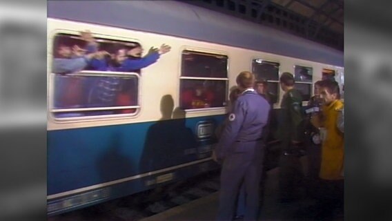 Menschen winken aus einem Zugwagon heraus. © NDR 