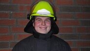 Lukas Tietböhl aus Elpersbüttel lächelt in Feuerwehr-Montur in die Kamera. © NDR Foto: Jörn Schaar