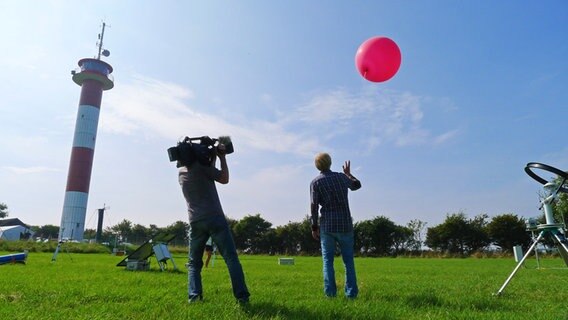 Ein Kameramann flimt wie ein junger Mann einen roten Ballon fliegen lässt © NDR Foto: Juliane Thomas