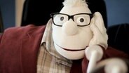 Die Handpuppe Werner Momsen sitzt vor einem Mikrofon. © NDR Foto: Janis Röhlig