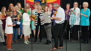 DIe Teilnehmer des friesischen Musikwettbewerbs stehen auf der Bühne und hören dem Moderator aufmerksam zu. © NDR Foto: Karin Haug