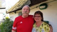 Gaby und Peter Gnau stehen lächelnd vor einem reetgedeckten Haus. © NDR Foto: Jörn Schaar