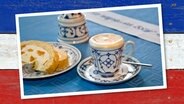 Pharisäer steht neben einem Stück Kuchen auf dem Tisch. Dahinter ein Holztisch in der Farben der Schleswig Holstein Flagge. © DUMONT Bildarchiv, binik Foto: DUMONT Bildarchiv, binik
