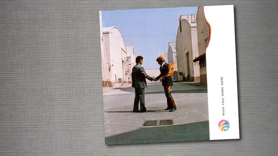 Das Cover zum Album "Wish you were here" von Pink Floyd zeigt zwei Männer im Anzug, die sich auf der Straße die Hände schütteln, wobei der Anzug eines Mannes brennt. © Harvest Foto: Harvest