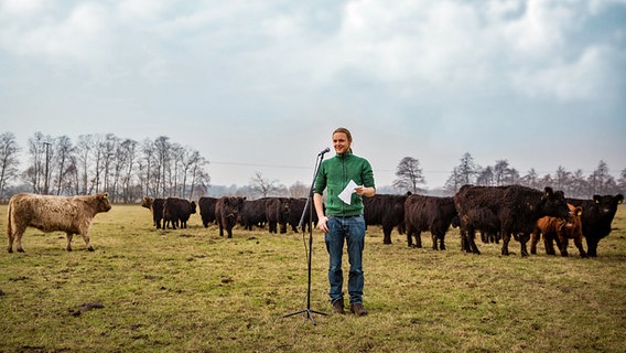 Eine junger Mann mit Pferdeschwanz steht vor einem Mikrofon auf einer Weide des Hofs Hartigswalde bei Neumünster. © Stiftung Naturschutz Schleswig-Holstein Foto: Jana Schmidt