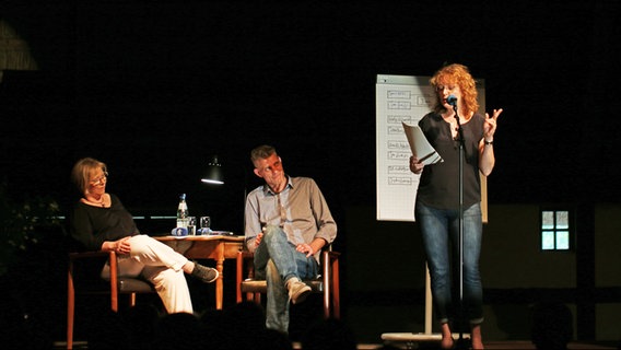 Neben NDR-Moderatorin Ines Barben und Autor Björn Högsdal steht Poetry Slammerin Ilka Brüggemann beim Poetry Slam op Platt auf einer Bühne in der Winkelscheune in Molfsee. © NDR Foto: Lornz Lorenzen
