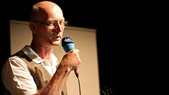 Poetry Slammer Jan Ladiges spricht auf einer Bühne in ein Mikrofon beim Poetry Slam op Platt in der Winkelscheune in Molfsee. © NDR Foto: Lornz Lorenzen