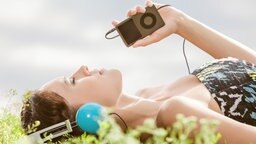 Eine Frau liegt auf einer Wiese und hört Musik. © fotolia.com Foto: Milch Images