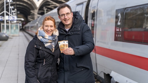 Die NDR-Moderatoren Mandy Schmidt (links) und Horst Hoof (rechts) stehen auf einem Bahnsteig und halten zwei 50-Euro-Scheine in den Händen. © NDR Foto: Janis Röhlig