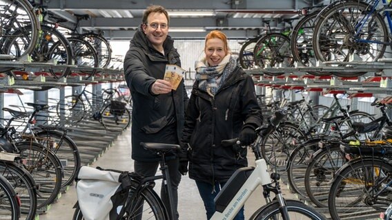 Die NDR-Moderatoren Horst Hoof (links) und Mandy Schmidt (rechts) stehen in einem Fahrradparkhaus und halten zwei 50-Euro-Scheine in die Kamera- © NDR Foto: Janis Röhlig