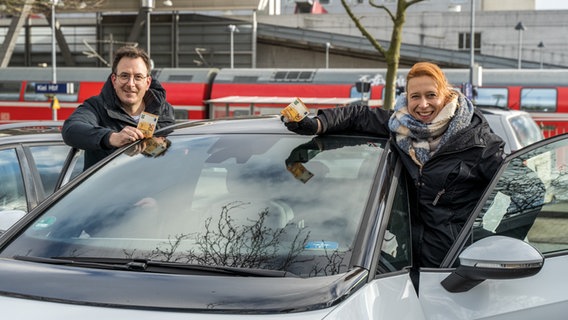 Die NDR-Moderatoren Horst Hoof (links) und Mandy Schmidt (rechts) stehen an einem Auto und halten einen 50-Euro-Schein in den Händen. © NDR Foto: Janis Röhlig