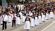 Männer und Frauen in Trachten ziehen bei einem Umzug über die Straßen und winken den Zuschauern.  Foto: Elin Rosteck