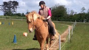 Eine Frau sitzt auf einem Pferd und reitet auf einem Reitplatz einen Sandweg entlang. © NDR Foto:  Elin Rosteck