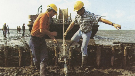 Altes Bild aus dem Kreisarchiv Nordfriesland, das zwei Männer mit Bauarbeiterhelmen vor einem Schleppkran zeigt. © Kreisarchiv Nordfriesland 