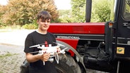 Samuel Lüdemann steht neben einem Trecker und hält dabei eine Drohne in der Hand. © NDR Foto: Peter Bartelt