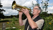 Peter Seifert aus Moorhusen steht im Freien und spielt Trompete. © NDR Foto: Peter Bartelt