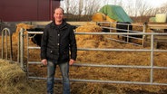 Andreas Frahm steht vor einem Rindergehäge auf einem landwirtschaftlichen Betrieb. © NDR Foto: Marie Meyer