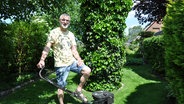 Ein Mann steht mit einem Rasenmäher im Garten.  