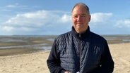 Jörn Sternhagen steht am Strand und lächelt in die Kamera. © NDR Foto: Nils Hansen