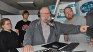 Dace Ellger, Jan Henning Stier, Andreas Guballa und Arndt Hauerken vom Offenen Kanal Westküste stehen in einem Hörfunk-Studio vor einem Mikrofon. © NDR Foto: Peter Bartelt