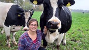 Lisa Suhr hockt neben einer großen Kuh und grinst in die Kamera. © NDR Foto: Lina Bande