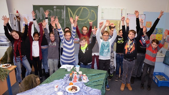 Mehrere Kinder stehen in einem Klassenraum und reißen gut gelaunt die Hände in die Luft. © NDR Foto: Katrin Bohlmann