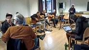 Eine Gruppe Menschen sitzt in einem Raum mit verschiedenen Musikinstrumenten. © NDR Foto: Annafried Stürmer