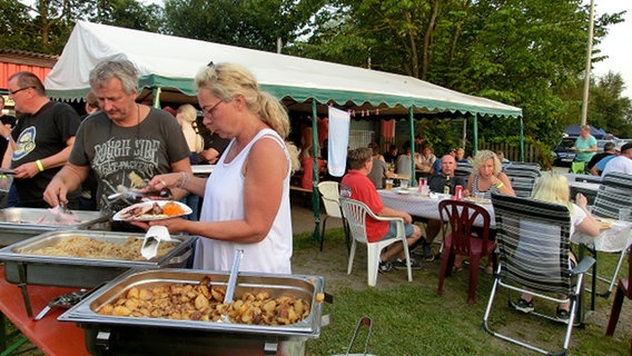 Menschen essen im Freien bei einem großen Zelt und Buffet im Freien. © NDR Foto: Dana Frohbös