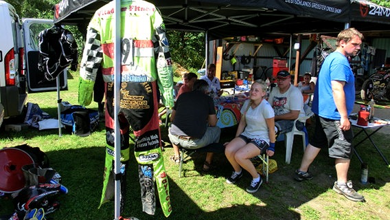 An einem Zelt hängen verschiedene Motorradanzüge für Speedway-Fahrer. © NDR Foto: Dana Frohbös