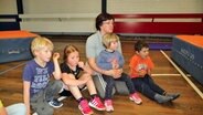 Die Jugendsportwartin des TSV Nordschwansen - Judith Henkel-  sitzt zwischen einigen Kindern in einer Turnhalle und hält ein Kind im Arm. © NDR Foto: Frank Hajasch